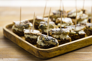 Small starter appetizers with canned fish and cream cheese on wooden tray on table background