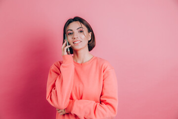 Photo of woman smiling while talking on smartphone isolated over pink background