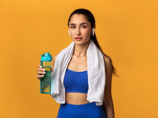Naklejka premium Confident sporty young woman holding water bottle at studio