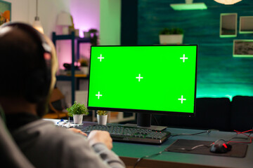 Concentrate gamer playing games on powerful computer with green mock up while streaming online competition. Player using pc with green screen isolated desktop streaming shooter games wearing headset