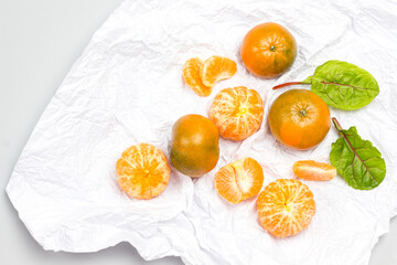 Tangerine wedges and a whole tangerine, chard leaves on white paper