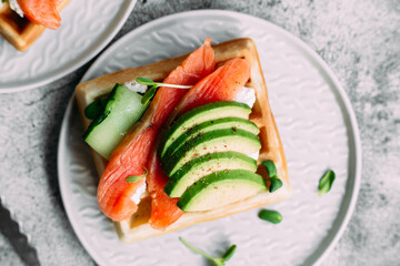 Belgian waffles with salmon, avocado and cream cheese on a white plate. Healthy breakfast at the table
