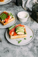 Belgian waffles with salmon, avocado and cream cheese on a white plate. Healthy breakfast at the table