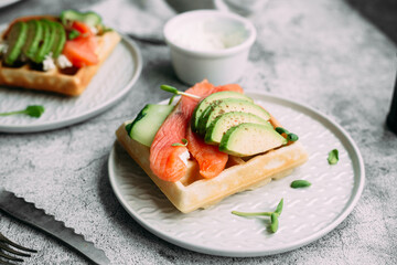 Belgian waffles with salmon, avocado and cream cheese on a white plate. Healthy breakfast at the table