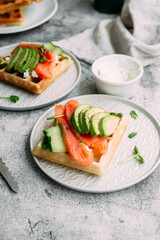 Belgian waffles with salmon, avocado and cream cheese on a white plate. Healthy breakfast at the table