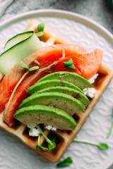 Belgian waffles with salmon, avocado and cream cheese on a white plate. Healthy breakfast at the table