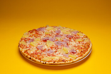 Dramatic spotlight on simple Hawai pineapple ham oven pizza with crunchy crest and golden orange tint. Studio food still life against a seamless yellow background