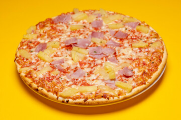 Tasty simple Hawai pineapple ham oven pizza with crunchy crest and orange tint filling the frame. Studio food still life against a seamless yellow background