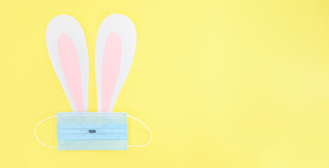 DIY concept. Top view of paper bunny ears and protective or medical mask on the yellow background. Easter and pandemic. Copy space, banner, place for text.