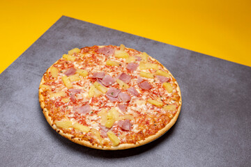 Modern kitchen gray surface with simple Hawai pineapple ham oven pizza with crunchy crest and golden yellow orange tint. Studio food still life against a seamless yellow background