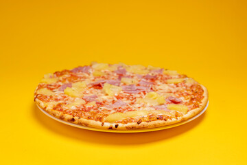 White space around simple Hawai pineapple ham oven pizza with crunchy crest and golden orange tint. Studio food still life against a seamless yellow background