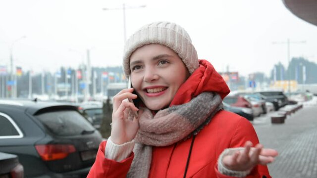 a cheerful young girl in a white hat and red coat talks on the phone outside