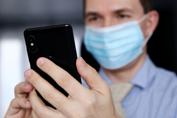 Smartphone in male hands close up, man in medical face mask and office clothes using mobile phone. Communication during coronavirus pandemic