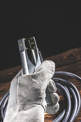 A welder in white welding gloves holds a wire with a ground terminal in his hand. Studio photo in...