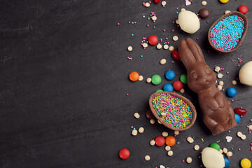 Fototapeta na wymiar Flat lay composition with chocolate Easter bunny, eggs and candies on black table. Space for text