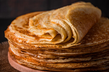 A stack of thin pancakes on a dark wooden background. A traditional dish of crepes for the holiday Maslenitsa.