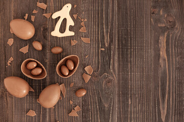 Flat lay of chocolate eggs, pieces of chocolate and candies and bunny on the wooden background. Handmade easter decoration. Copy space, place for text. Eater gift.
