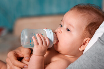Close up portrait of baby eating from a bottle. Side view. Concept of infant feeding and weaning