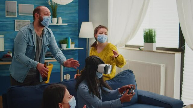 Black woman experiencing virtual reality headset playing video games wearing face mask while friends having fun drinking beer. respecting distancing wearing face mask to prevent infection with virus,