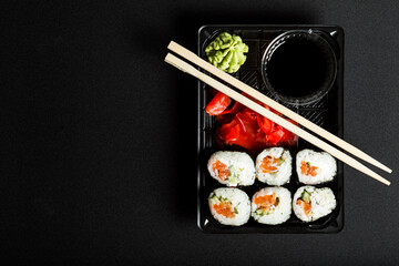 Plastic container with sushi set. Sushi set to go on black. Sushi on black background with copy space.
