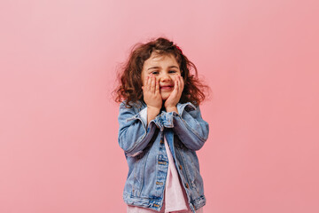 Adorable cute kid in denim jacket touching face. Smiling preteen girl posing on pink background.