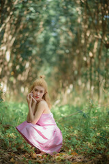 Lovely young lady wearing pink dress sit and rest in woods.