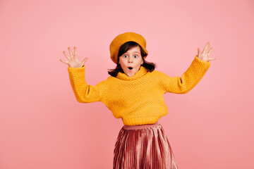 Funny child jumping with hands up. Studio shot of carefree preteen girl in yellow sweater.