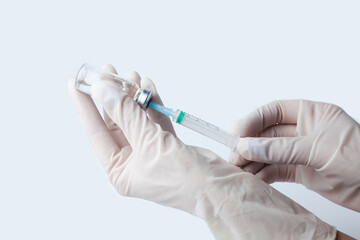 Doctor's or nur's hand in white protective gloves hold syringe with preparation for injection on the white background. Influenza and coronavirus vaccination. Close-up. Copy space.