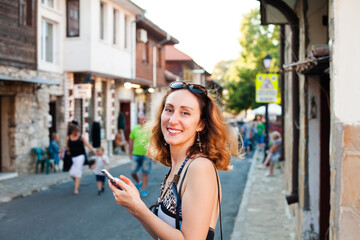 Happy young woman smiling and walking in the street using a smartphone. Summer vacation. Bulgaria. Nessebar.