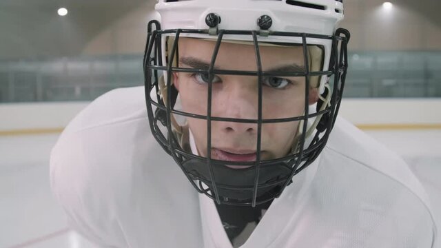 Close up arc portrait with slowmo of young handsome male hockey player in helmet with cage standing on empty ice arena looking at camera