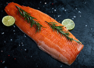 A piece of fresh cut salmon with rosemary on a dark textured background.