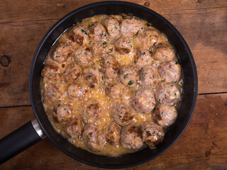 Chicken meatballs with cheese in a creamy sauce in a frying pan on a wooden kitchen table, top view, close-up - Swedish cuisine