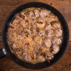 Chicken meatballs with cheese in a creamy sauce in a frying pan on a wooden kitchen table, top view, close-up - Swedish cuisine