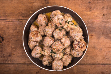 Chicken meatballs with cheese in a creamy sauce in a bowl on a wooden kitchen table, top view, close-up - Swedish cuisine