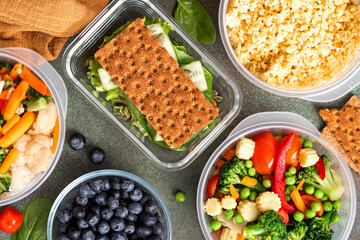 Various food in plastic and glass containers. Salad, bulgur, sandwiches and berries in plastic containers on a dark background. Top view. Food storage, takeaway
