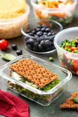 Various food in plastic and glass containers. Salad, bulgur, sandwiches and berries in plastic containers on a dark background. Food storage, takeaway