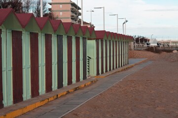 Green beach huts and cabins on the sand with wooden door and red roofs (Pesaro, Italy, Europe)