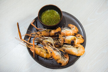 Grilled river shrimps with chili seafood sauce on black plate on wooden table.