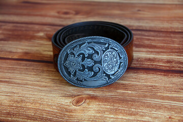 Leather cowboy belt with oval patterned buckle on a wooden background