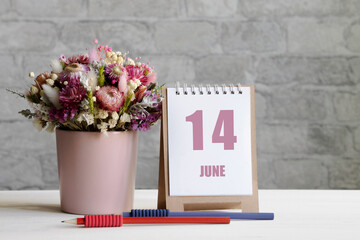 june 14. 14th day of the month, calendar date.A delicate bouquet of flowers in a pink vase, two pencils and a calendar with a date for the day on a wooden surface