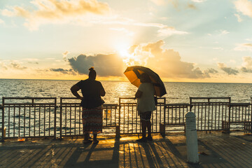 two women black race sunrise pier umbrella sun summer sky clouds sea pier