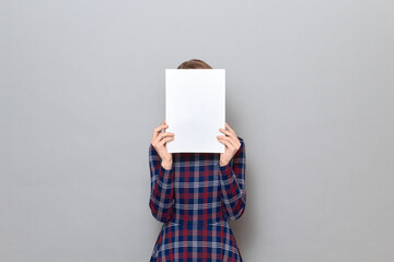 Woman is holding white blank paper sheet in front of her face