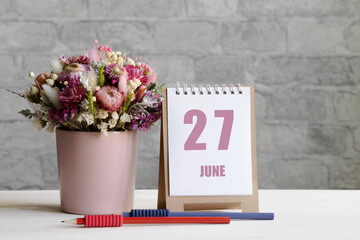 june 27. 27th day of the month, calendar date.A delicate bouquet of flowers in a pink vase, two pencils and a calendar with a date for the day on a wooden surface