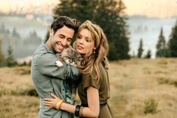Beautiful sensual couple hug together with the cat and smile cheerfully in nature.