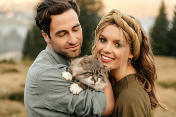 Beautiful sensual couple hug together with the cat and smile cheerfully in nature.