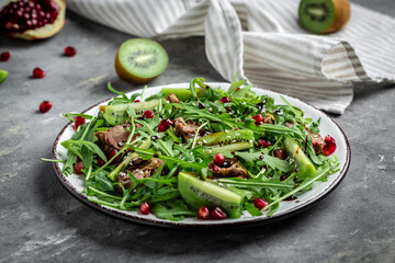 Grilled chicken liver and fresh vegetable salad of lettuce, arugula, kiwi and pomegranate. top view
