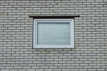 one white square window on a gray brick wall of a building