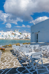 Cycladitic view of a cafe exterior and  whitewashed houses with the christian church of kimisis Theotokou as a background   in Naousa  Paros island, Greece