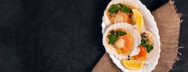 Baked scallops with caviar and creamy garlic sauce in white plate. Scallops with lemon on black background with napkin. Top view. Copy space.