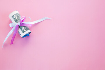 Rolled up dollar bills secured by blue and pink ribbon with copy space on a pink background